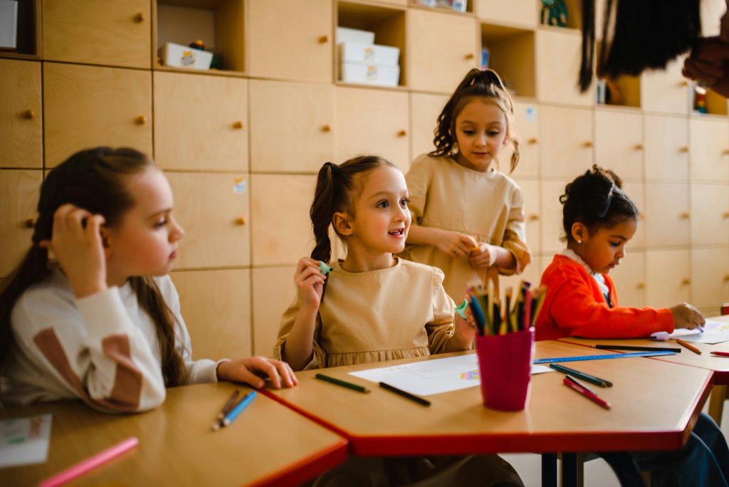 A group of children sitting together at school desks, drawing and smiling, representing how children with autism build friendships in supportive classroom settings