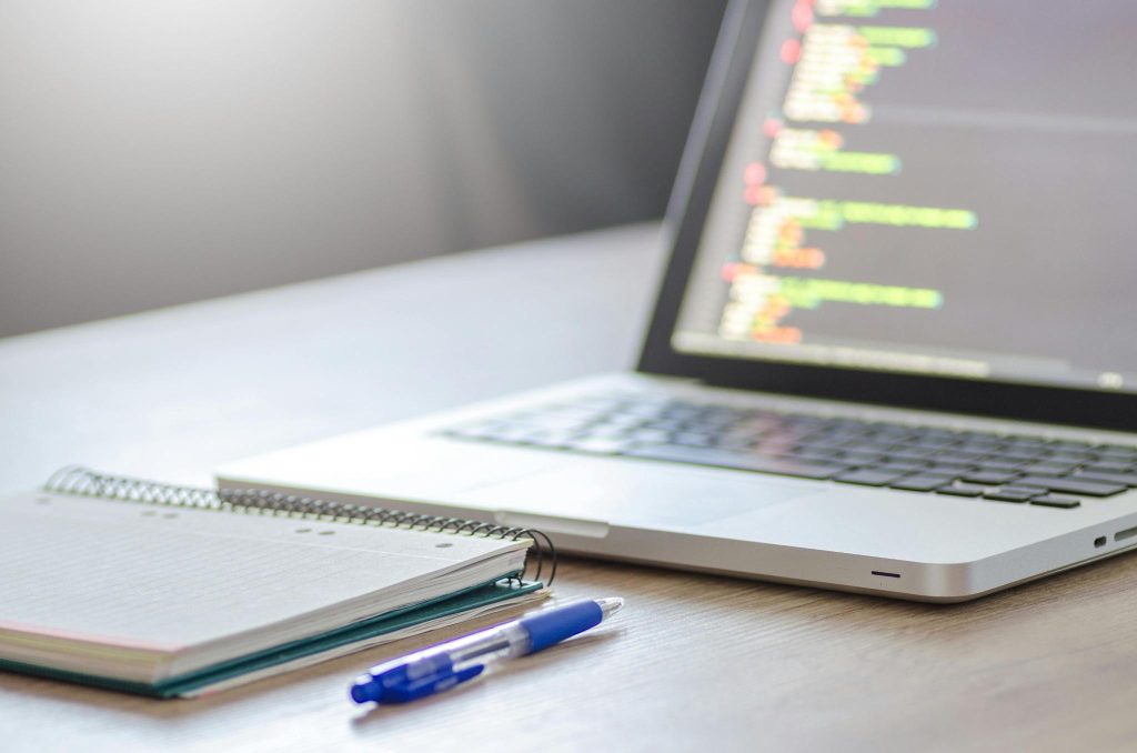 Open laptop with coding screen and notebook illustrating ABA Artificial Intelligence technology development.