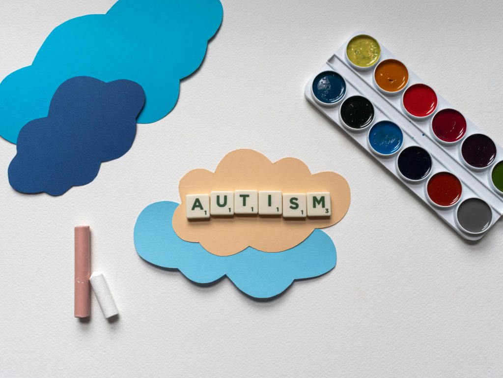 Educational art setup with pastel clouds and Scrabble tiles spelling “autism,” supporting the blog topic “what is the autism creature.